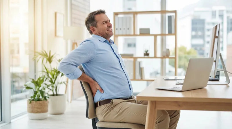 Desk worker at an office with lower back tightness after prolonged sitting — the front of the hips is often worth checking